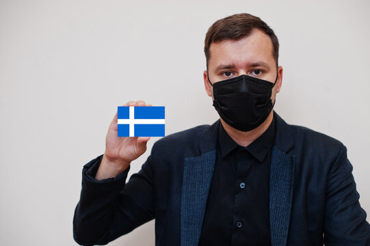 Man wear black formal and protect face mask, hold Shetland flag card isolated on white background. United Kingdom counties of Scotland coronavirus Covid concept.