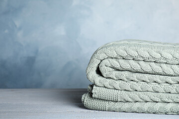 Knitted plaid on light grey wooden table, closeup. Space for text