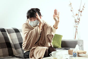 Fototapeta premium Woman wrapped in a plaid, wearing face mask trying to protect herself from somebody's sick near by, looks disguasted, angry, sad sitting on sofa at home indoors. Healthcare and medicine, ill