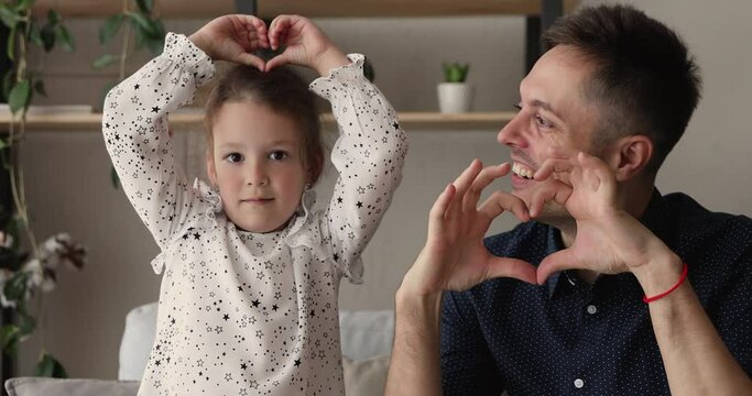 Young father and little 5s adorable daughter smiling looking at camera showing symbol making with fingers heart shape sign of love. Concept of blood donation and save life, volunteering, family bond