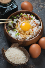 Wooden bowl with tamago kake gohan or japanese rice with a raw chicken egg, vertical shot, selective focus