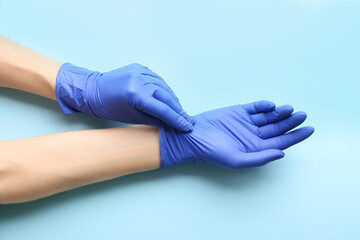 Person putting on medical gloves against light blue background, closeup of hands