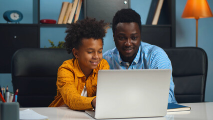 African father with son enjoying family time together at home playing game on laptop