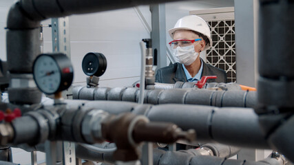 Maintenance engineer in safety mask checking technical data of heating system equipment at factory