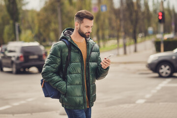 Profile side photo of cute confident young guy dressed green coat rucksack walking chatting modern gadget outdoors city street © deagreez