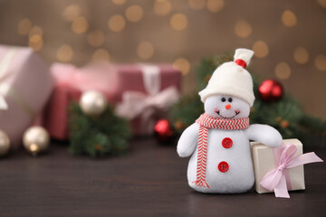 Snowman toy and Christmas box on table against blurred festive lights. Space for text