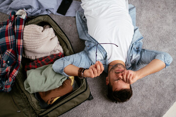 Young smiling man packing clothes into travel bag. Man preparing for the trip.