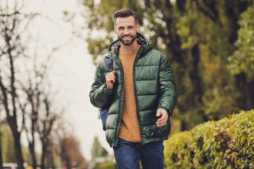 Photo of satisfied person carry bag smile look camera unzipped clothing free time walking outdoors