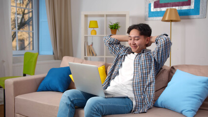 Young asian man sitting on couch and using laptop at home