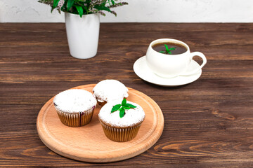Cupcakes with black currants on a background of flowers and mint leaves, on a round board on a wooden background.