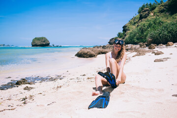 Happy woman putting on flippers for diving while sitting on beach © BullRun