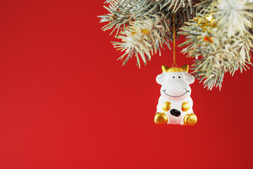 Figure of a Cow on a spruce branch, on a red background.
