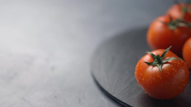 Farm tomatoes on a dark plate and a dark background move along the frame. Place for text. Close-up
