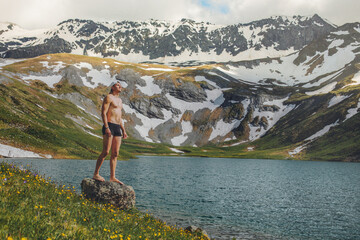 Tourist in a bathing suit standing up on the shore of a pure mountain lake