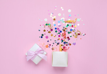 Shiny colorful confetti bursting out of box on pink background, top view