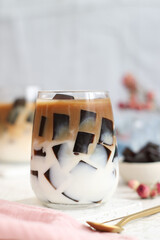 A glass of iced milk latte with milk, fresh homemade Japanese coffee jelly with golden color spoon in background. It's a dessert flavored with coffee, gelatin and sugar.