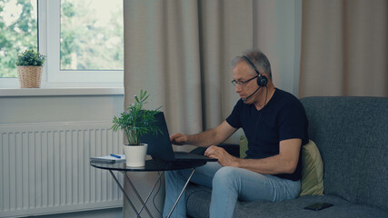 A man with headphones is working at a computer at home.