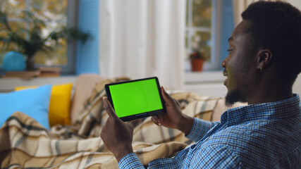 African man with tablet computer having video call and resting on couch at home
