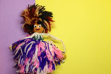 A loose wool doll wearing purple, white pink dress and beaded head over purple and yellow background with text space