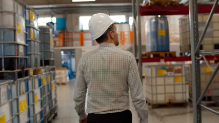 Back view of male manager in helmet walking in industrial warehouse