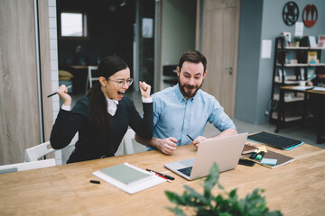 Woman raising hands screaming with joy near man in office