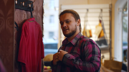 Obraz premium Young man choosing shirt and looking to mirror in mall