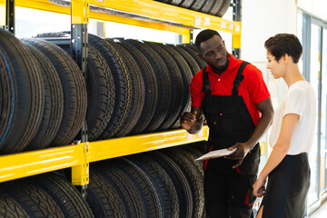 Black male salesman showing wheel tires to caucasian woman customer at car repair service and auto...