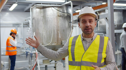 Foreman in safety hardhat having online tour in chemical factory looking at camera and talking