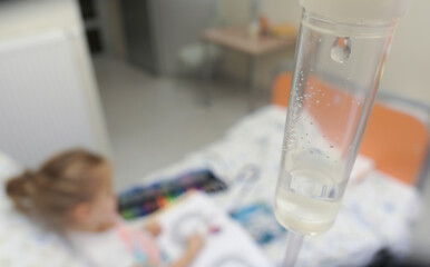Young Girl on a Drip with Peripheral Venous Catheter Reading Book in Hospital