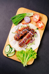 Grilled lula kebab on pita bread with vegetables on a dark background