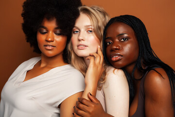 Obraz premium young pretty caucasian, afro, scandinavian woman posing cheerful together on brown background, lifestyle diverse nationality people concept