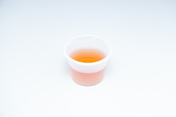 Small transparent plastic medicine drinking cup with orange colored liquid isolated on white