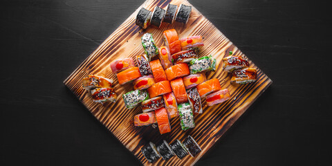 set of sushi roll with salmon, avocado, cream cheese, cucumber, rice, caviar, eel, tuna in wooden plate on black background