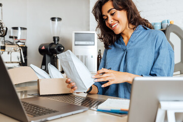 Beautiful cafe owner holding a white pack of coffee. Young entrepreneur receiving a parcel with...