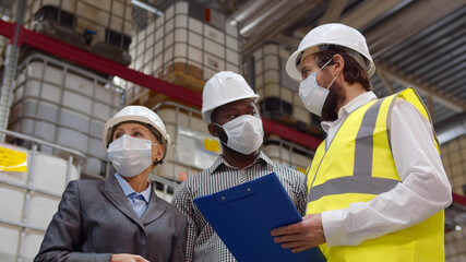 Diverse warehouse inspectors wearing safety mask discussing distribution plan on clipboard - Powered by Adobe