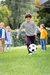 Asian boy playing football near friends in park at background