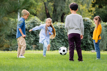 Girl playing football with friends on blurred foreground in park