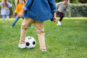 Boy playing football with friends on blurred background on lawn