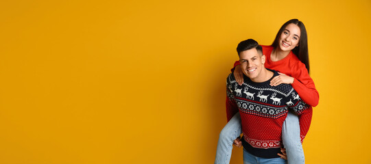 Couple in Christmas sweaters on yellow background, space for text