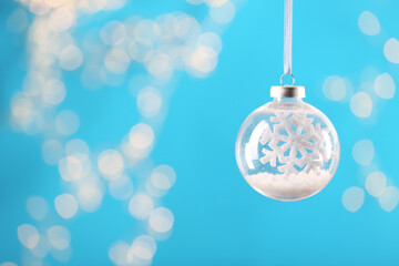 Decorative snow globe hanging on against blurred festive lights, space for text