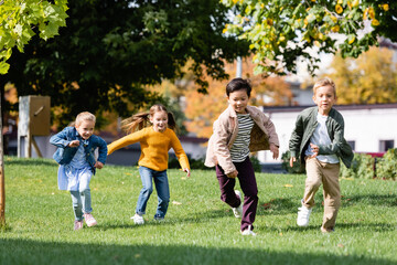 Smiling multiethnic children running on grass in park
