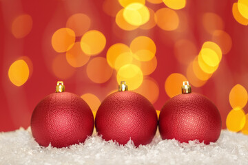 Beautiful red Christmas balls on snow against blurred festive lights, space for text