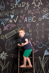 a small child climbs the stairs near the chalk-painted slate wall. three-year-old boy learns to draw flowers. art school.