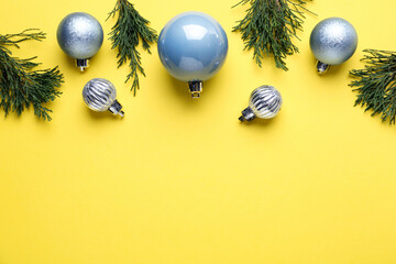 Beautiful blue Christmas balls and fir branches on yellow background, flat lay. Space for text