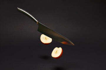 A  kitchen knife in gravity cuts an apple in half isolated on black background.