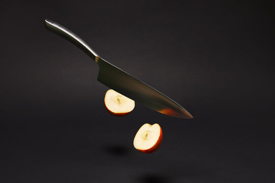 A  Kitchen Knife In Gravity Cuts An Apple In Half Isolated On Black Background.