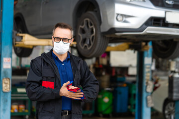 Fototapeta na wymiar Portrait of caucasian man Cleaning Hands With Cloth and wearing medical face mask protection coronavirus.. Expertise mechanic working in automobile repair garage.