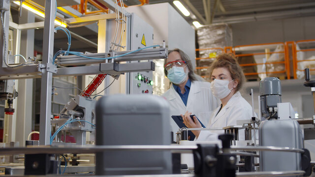 Operators in safety mask and lab coat controlling production line from control panel