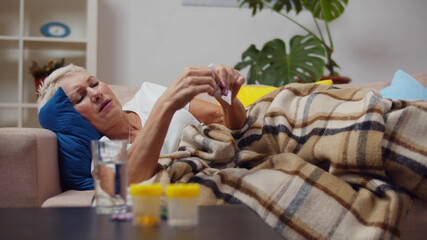 Elderly woman suffering from pain and taking pills lying on couch