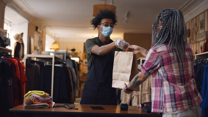 Young woman in safety mask purchasing in clothes store